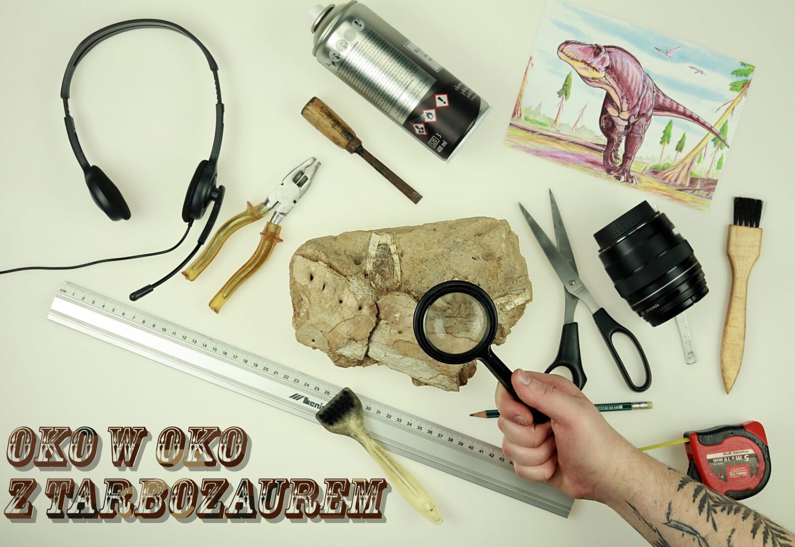 Widok z góry na różne narzędzia i przyrządy: od lewej słuchawki, kombinerki, dłutko, spray, rysunek dinozaura, nożyczki, skamienielina, lupa, metr i miarka
