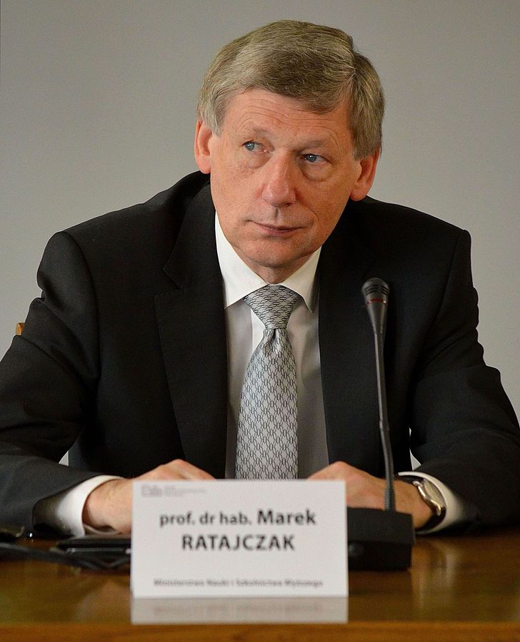 mężczyzna w średnim wieku w marynarce siedzący przy biurku z mikrofonem