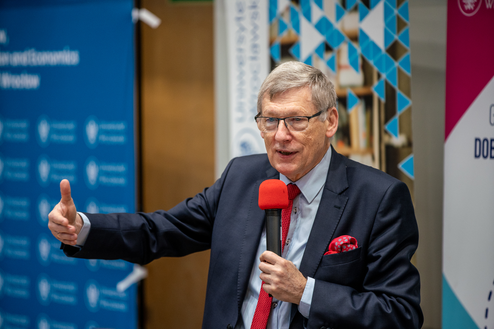 starszy mężczyzna w garniturze z czerwonym mikrofonem mówiący