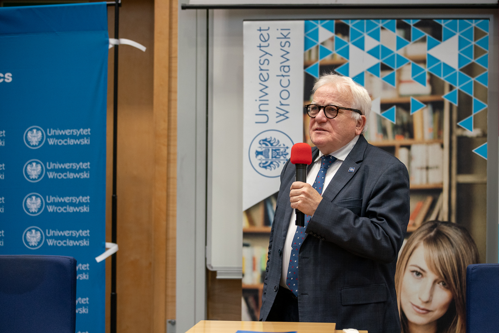 starszy siwy mężczyzna w marynarce trzymający czerwony mikrofon