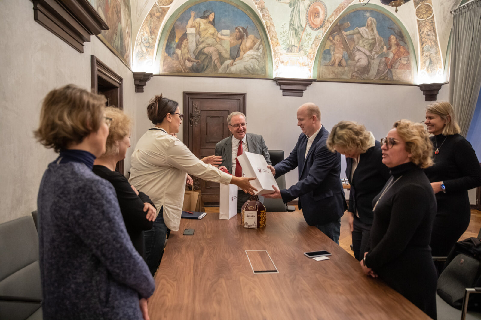 grupa osób przekazująca sobie prezenty, stojąca przy stole