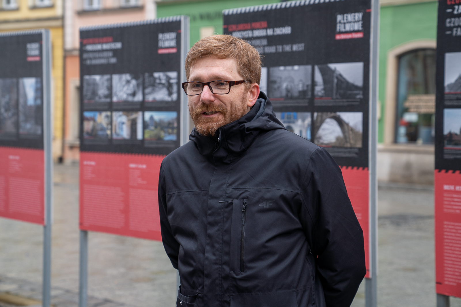 Mężczyzna z brodą w okularach, za nim wysstawa