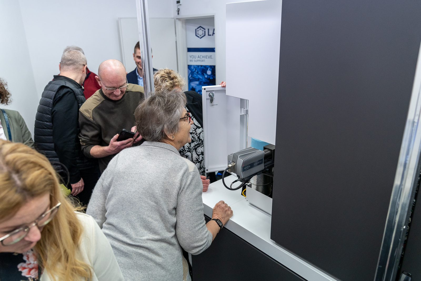 kilka osób zgromadzonych wokół dużego, biało-szarego urzadzenia