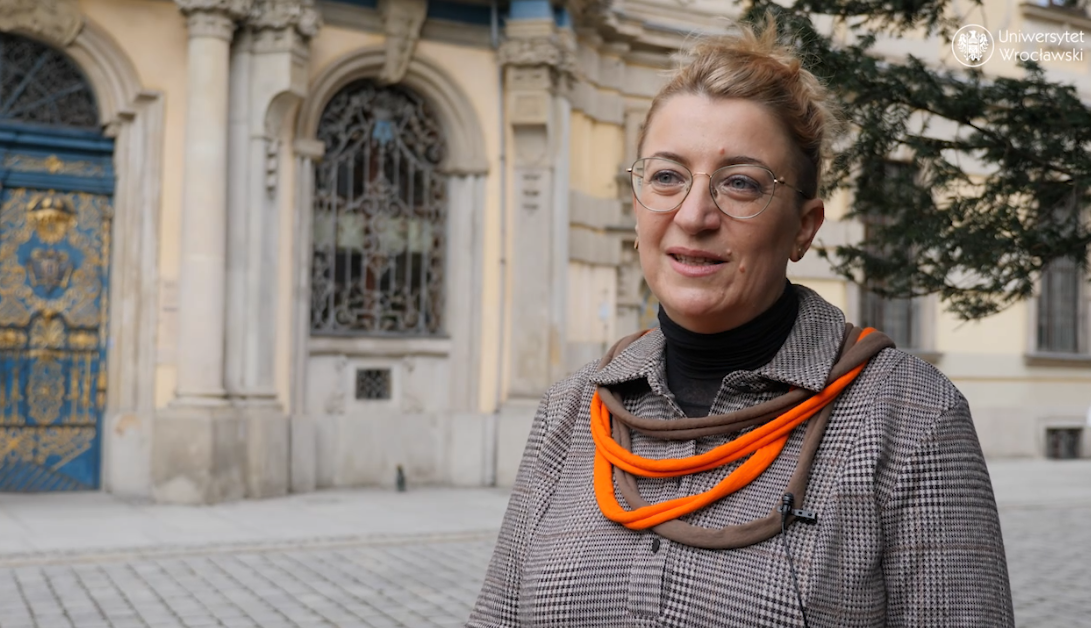 kobieta z okularami, biżuterią, płaszczu na tle uniwersytetu