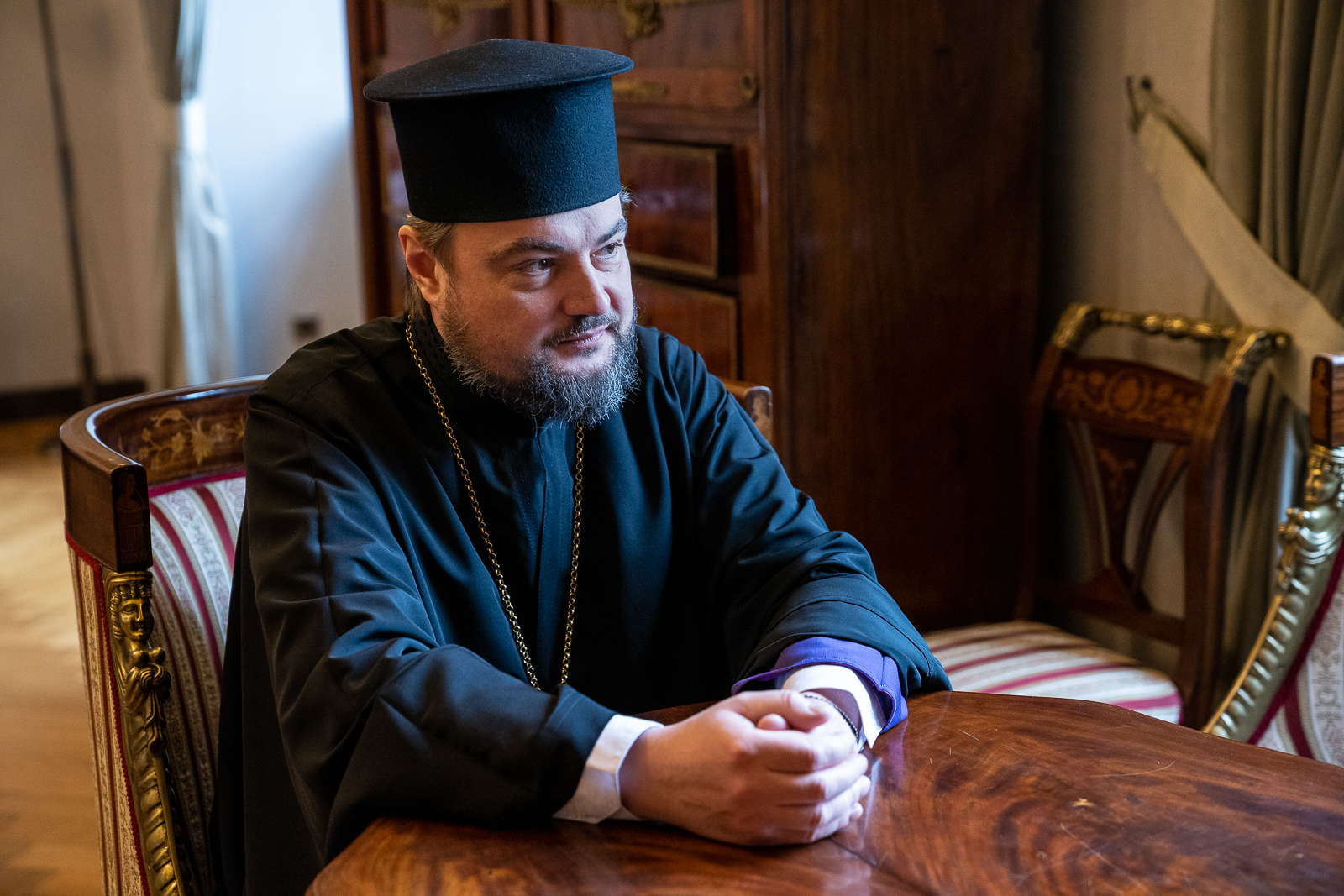 brodaty mężczyzna w czarnym stroju i czarnym nakryciu głowy siedzi przy stole