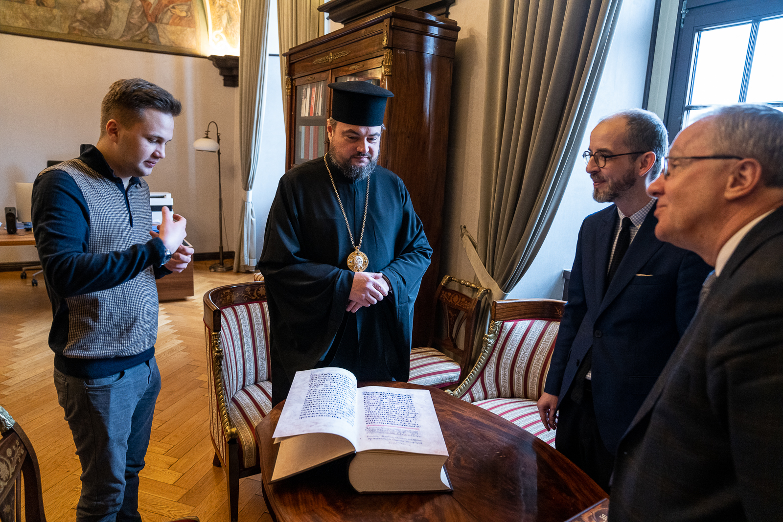 czterej mężczyźni przy stole, na którym lezy gruba księga
