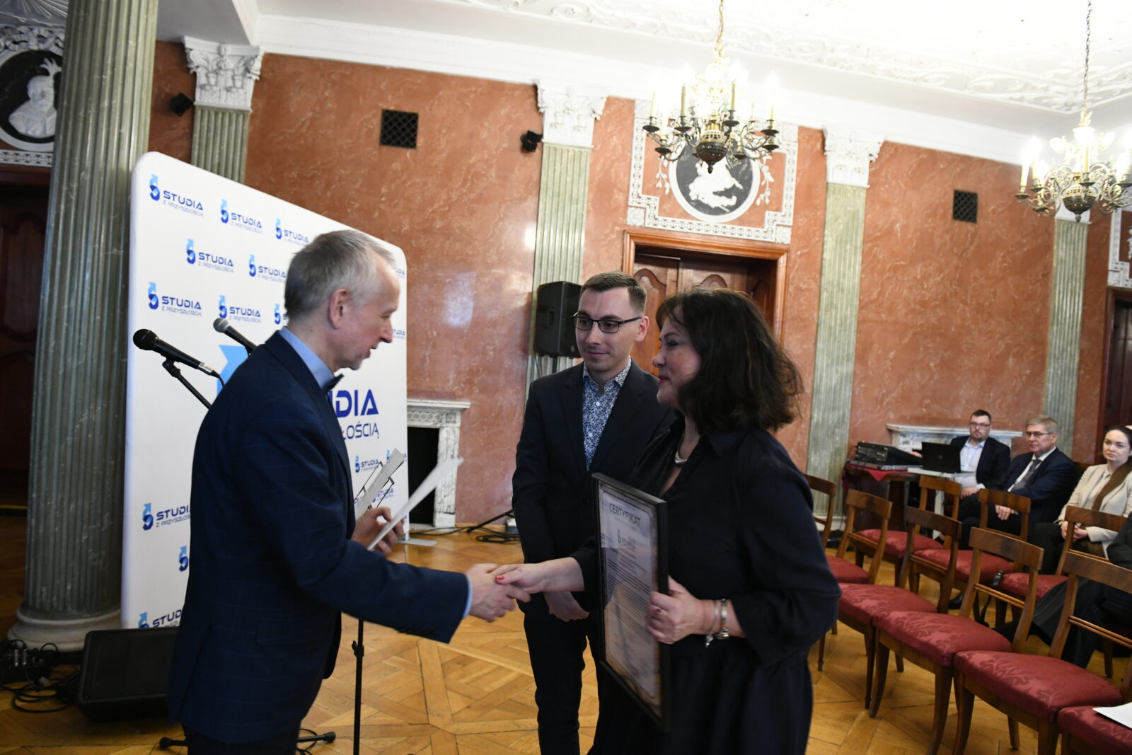 młody mężczyzna i kobieta w średnim wieku którym podaje rękę starszy mężczyzna