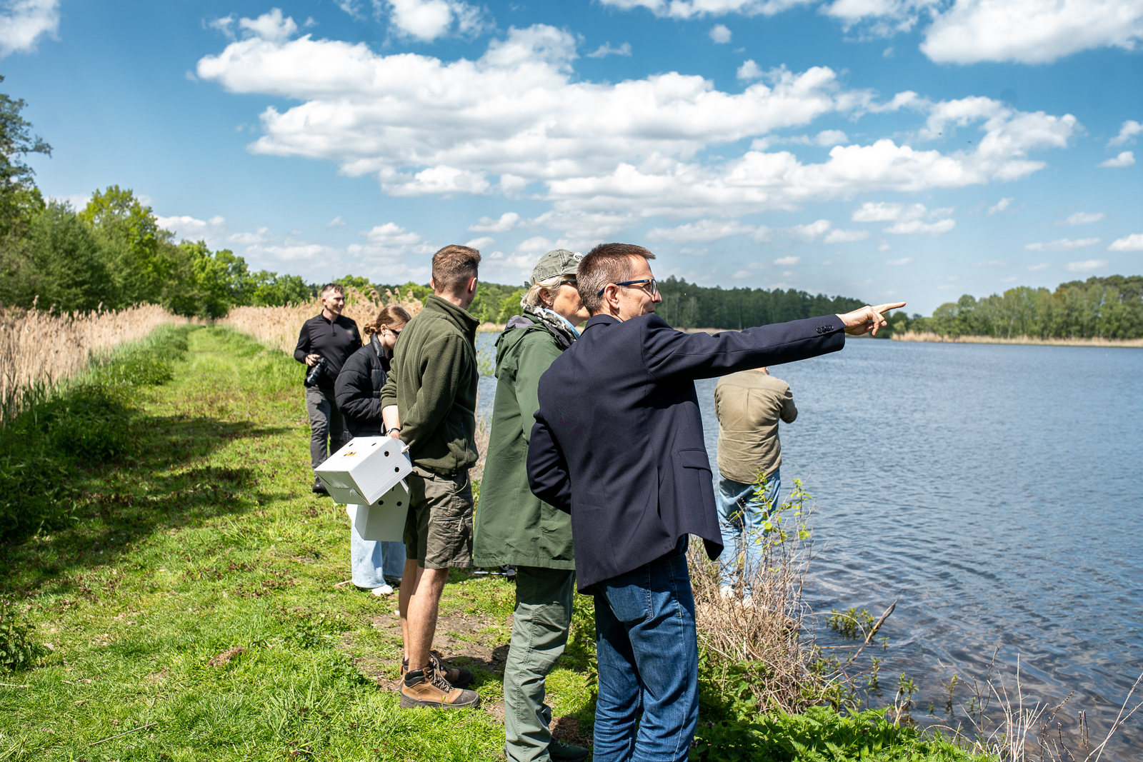 kilka osób stojących w trawie patrzących w dal nad wodą
