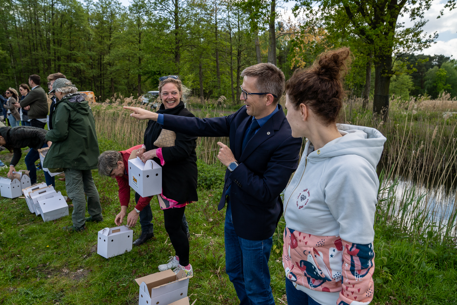 kilka osób stoi w trawie, obok nich otwarte i zamknięte kartonowe pudełka