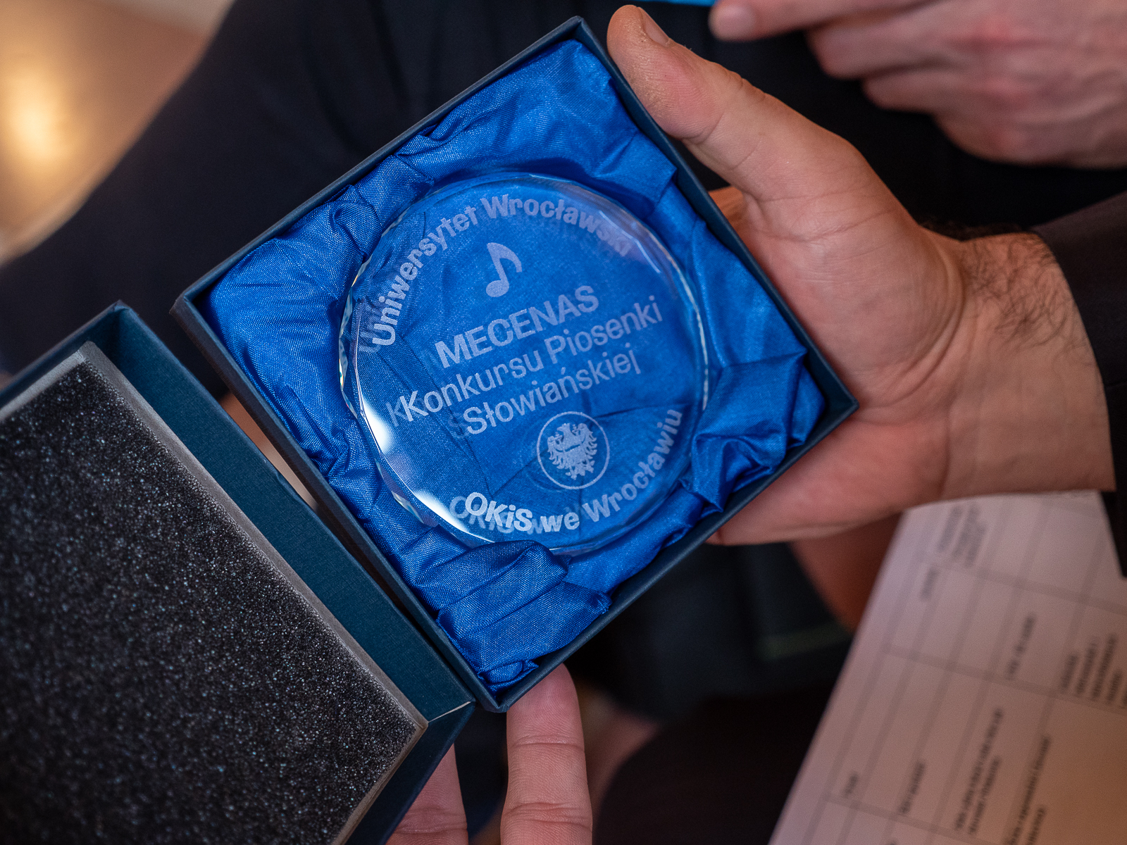 Okrągły szklanu medal w pudełku z niebieską wyściółką.