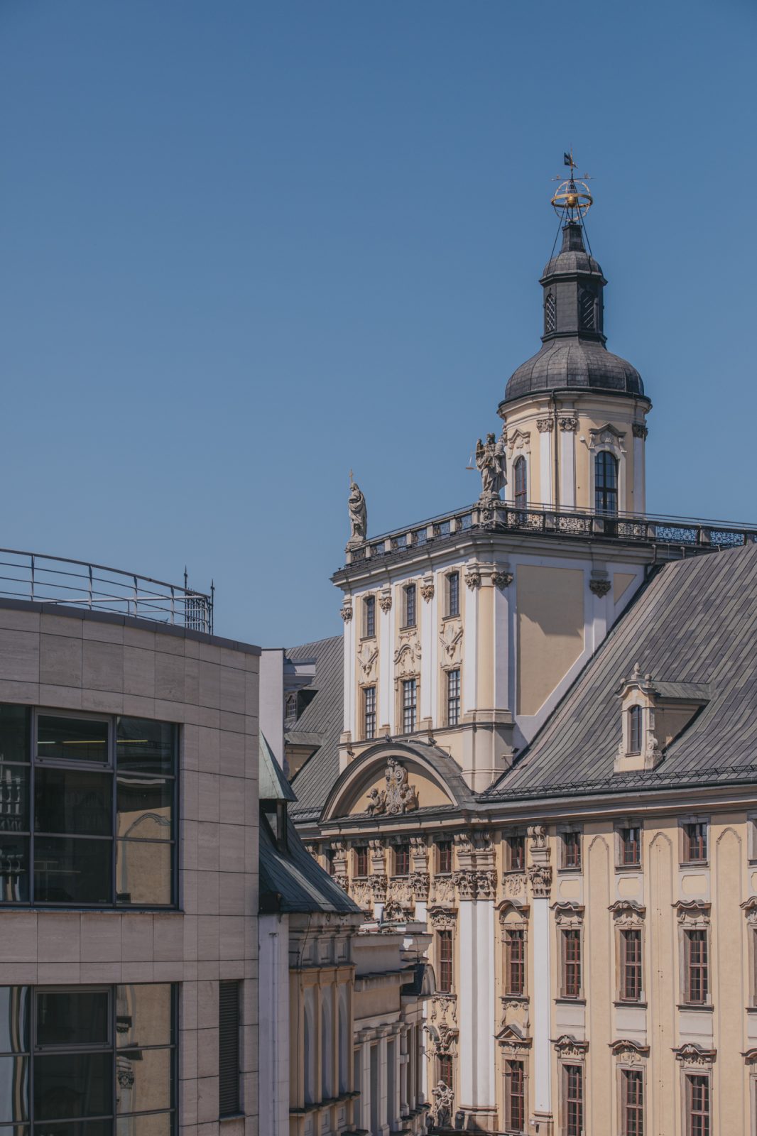 dwa budynki, jeden nowoczesny, drug z wieżą, nad nimi bezchmurne niebo