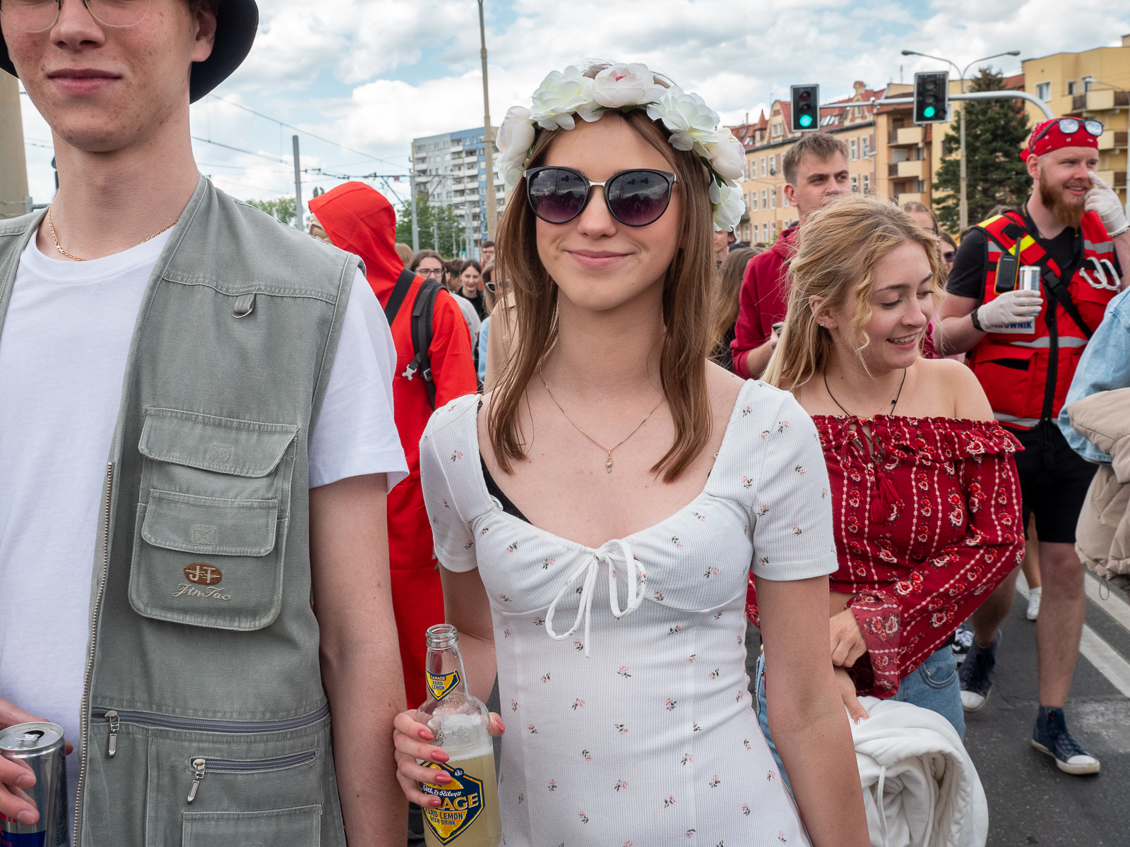 Ludzie idący w pochodzie juwenaliowym ulicami Wrocławia. Na pierwszym planie studentka w białej bluzce z białym wiankiem z kwiatów na głowie.