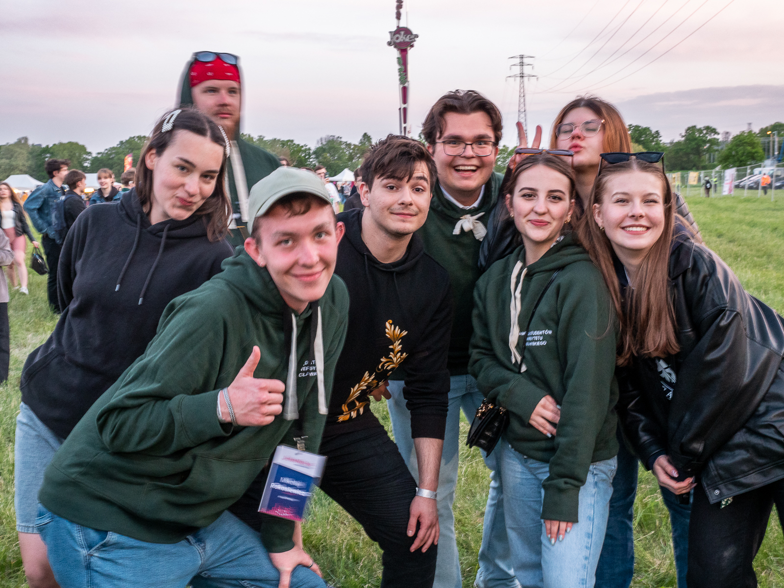 Grupa uśmiechniętych studentów i studentek pozująca do zdjęcia na polu koncertowym.