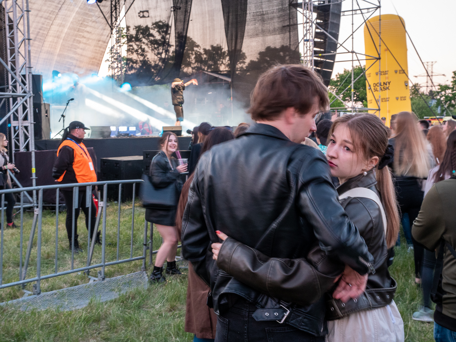 Przed sceną, na której odbywa się koncert stoi para - student i studentka, obejmują się.