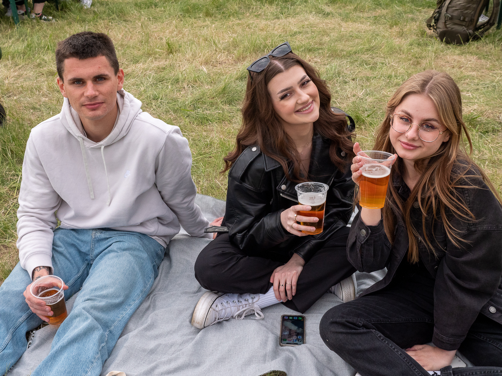 Dwie studentki i student siedzący na kocu na trawie.