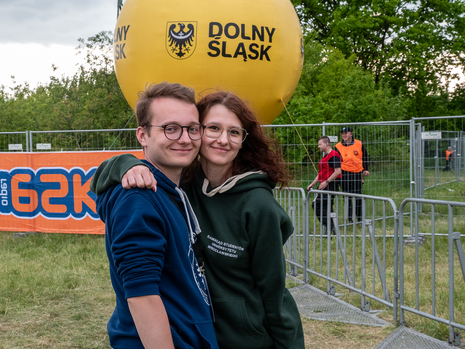 Student i studentka, uśmiechnięci, w okularach. Ona trzyma go za ramię, zbliżają się policzkami.