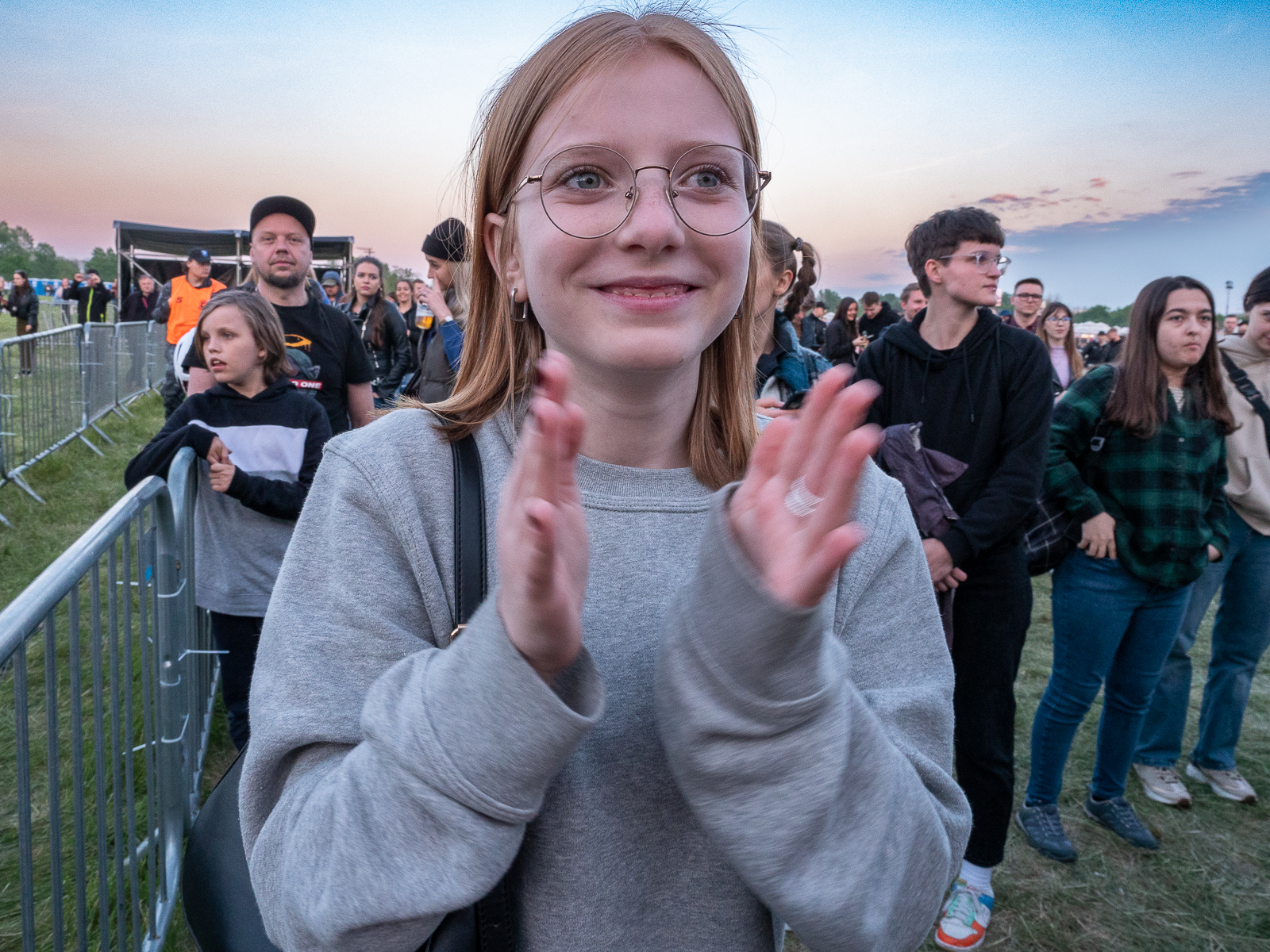 uśmiechnięta dziewczynka w okularach klaszcząca w ręce. za nią publiczność.