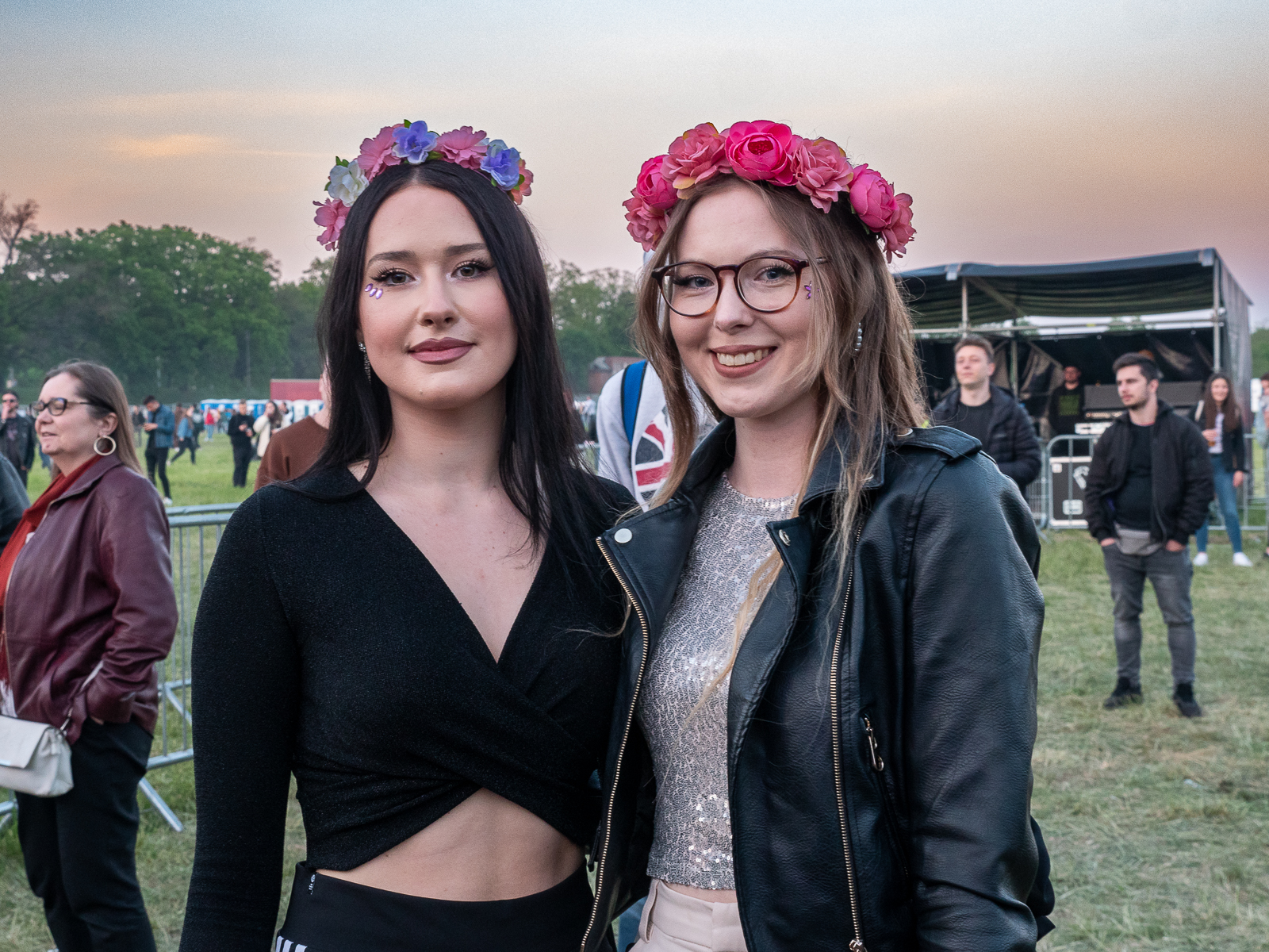 dwie uśmiechnięte studentki z wiankami z kwiatów na głowie stoją na trawie, za nimi dwóch mężczyzn, obok dalej kobieta