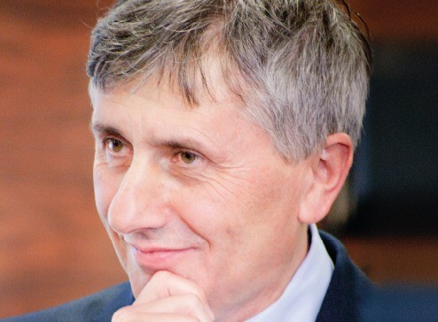 mężczyzna w starszym wieku o siwych włosach w białej koszuli i granatowej marynarce