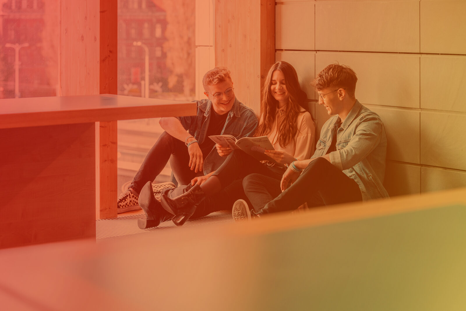 Troje studentów siedzi na podłodze pod ścianą