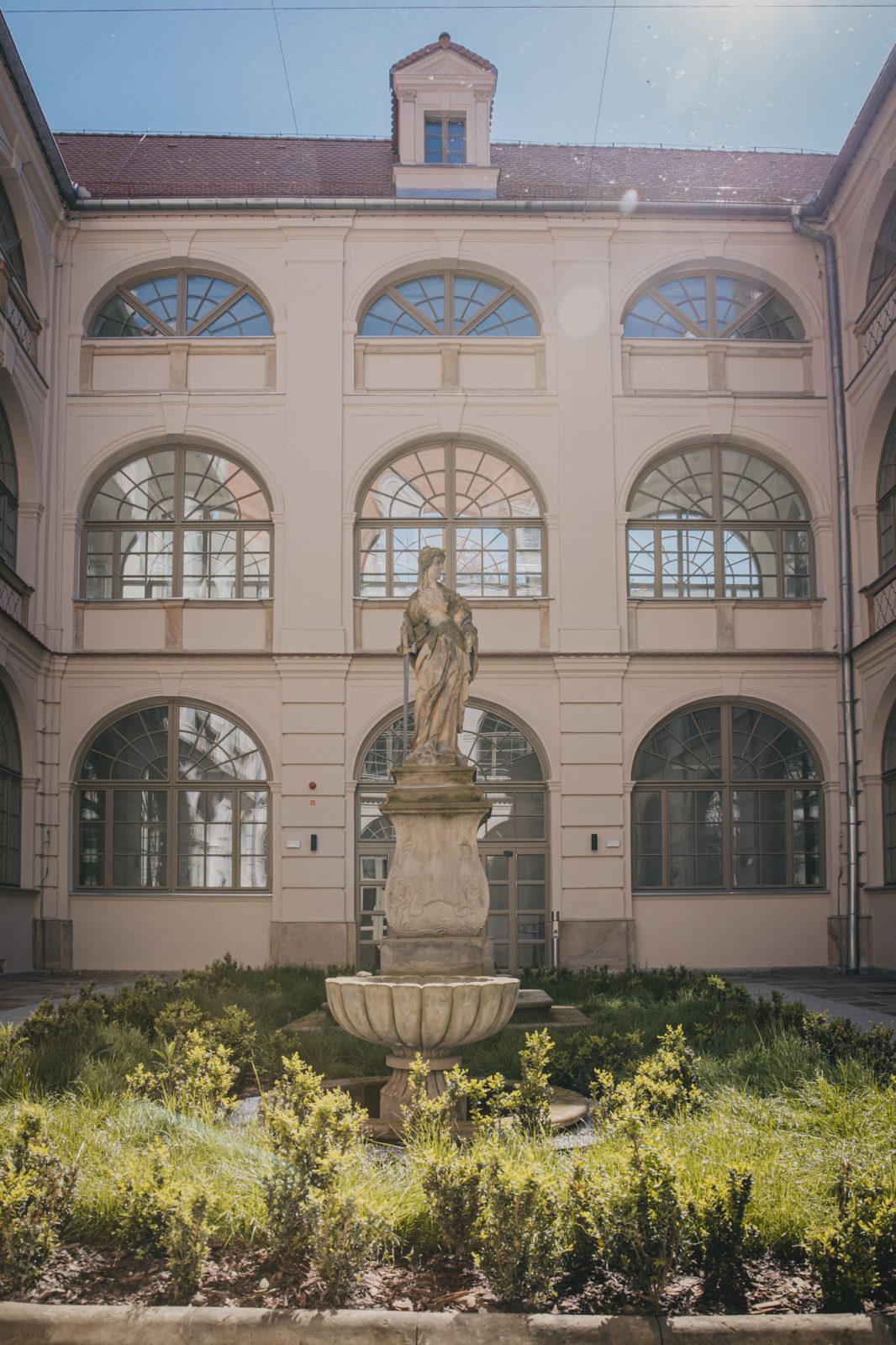 zabytkowa figura, w tle zabytkowy budynek z półokrągłymi oknami