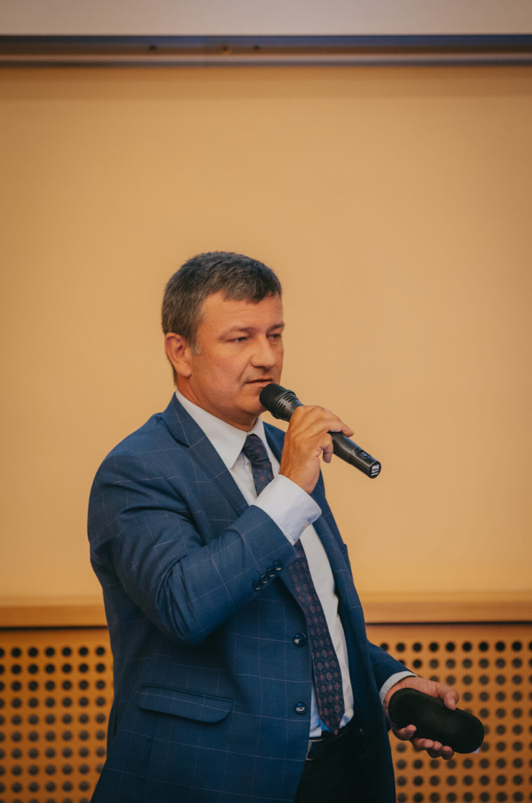 mężczyzna w średnim wieku ubrany elegancko przemawiający do publiczności
