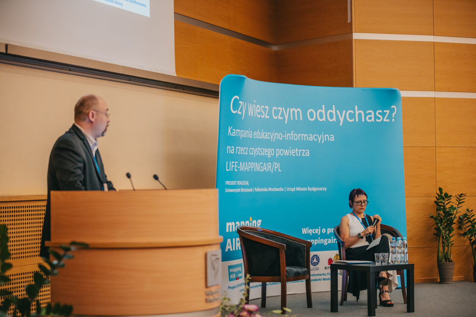 dwie osoby na scenie przemawiające do publiczności