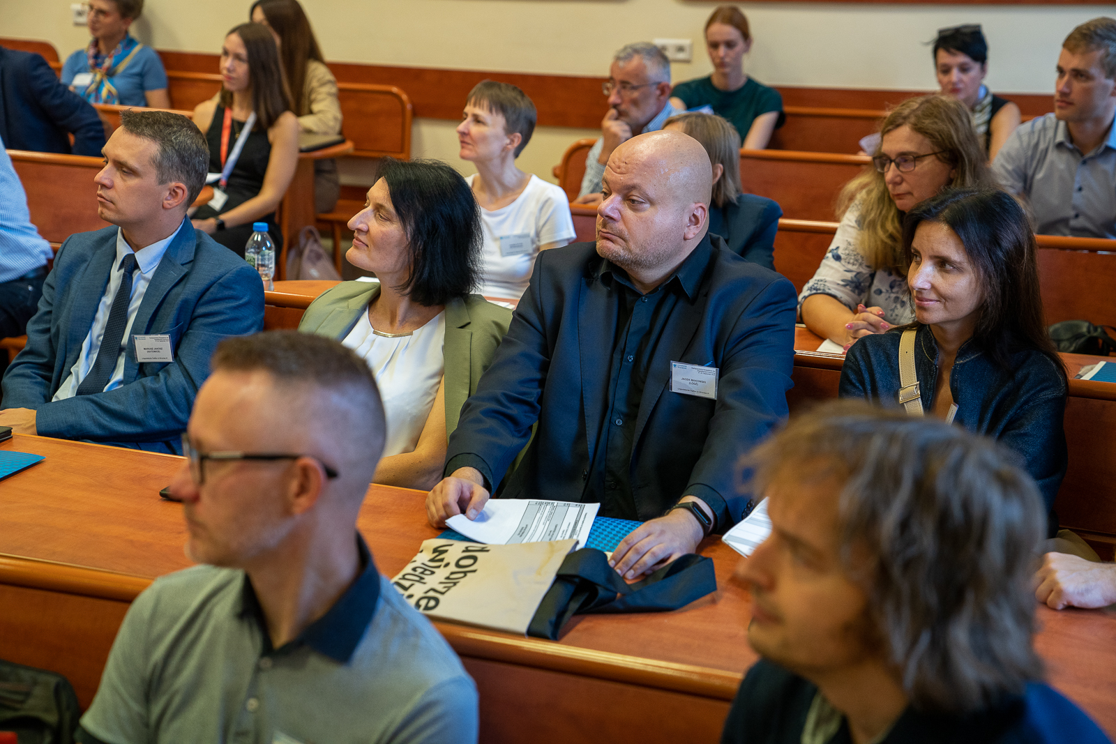 grupa ludzi siedząca w ławkach na sali konferencyjnej