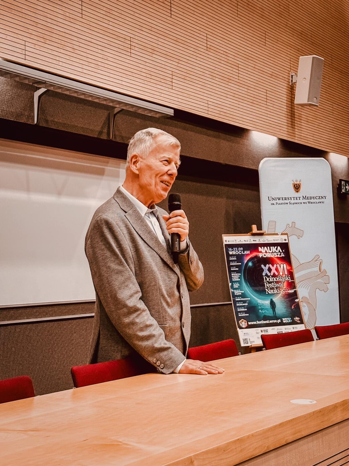 Prof. Jan Miodek - starszy mężczyzna mówiący do mikrofonu.