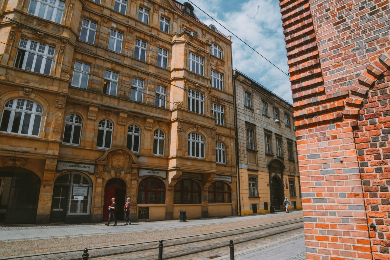 Kilkopiętrowe, żółte i szare kamienice z licznymi oknami, stojące przy brukowanej ulicy
