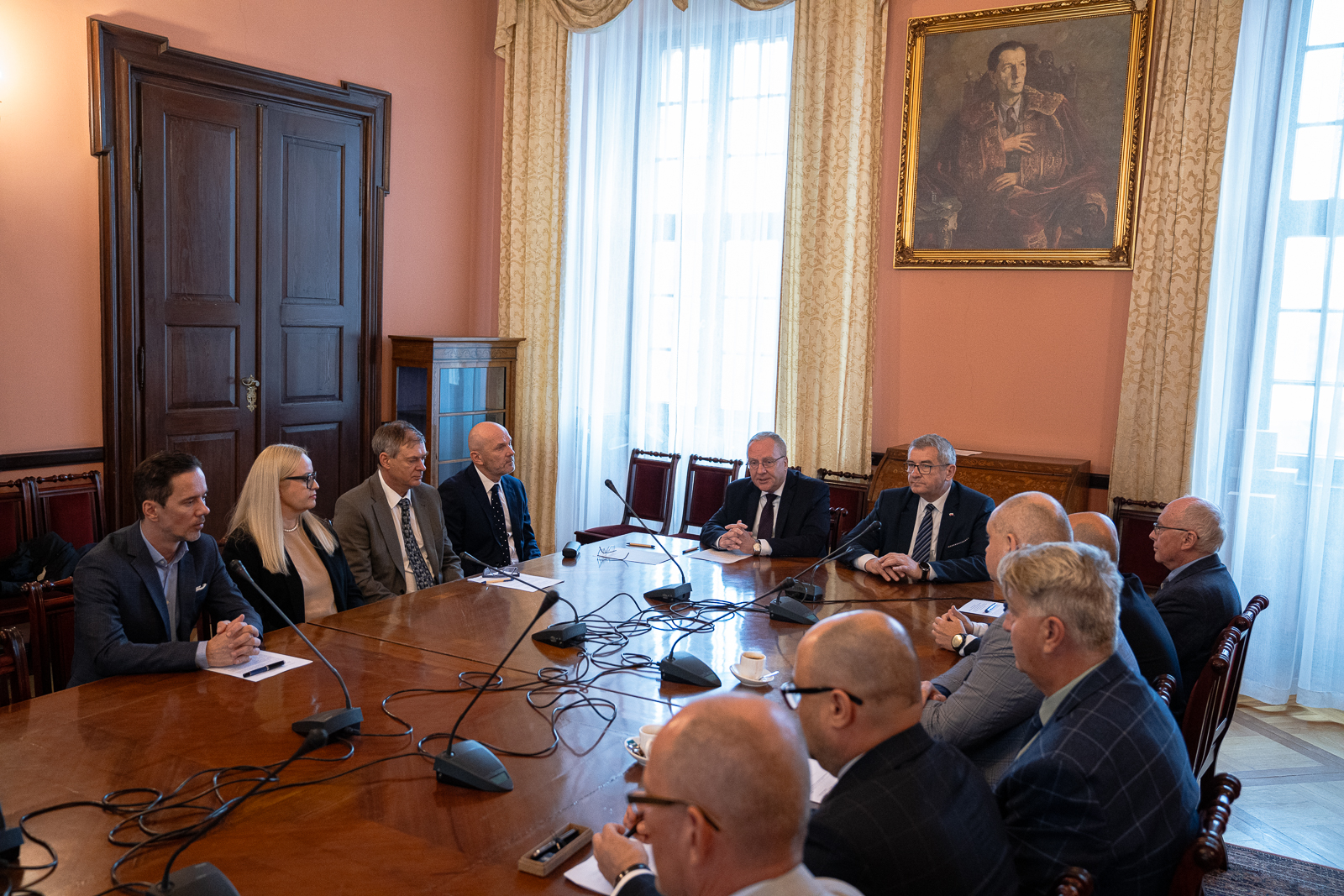 grupa mężczyzn w starszym wieku oraz kobieta siedząprzy dużym stole , na którym stoją mikrofony