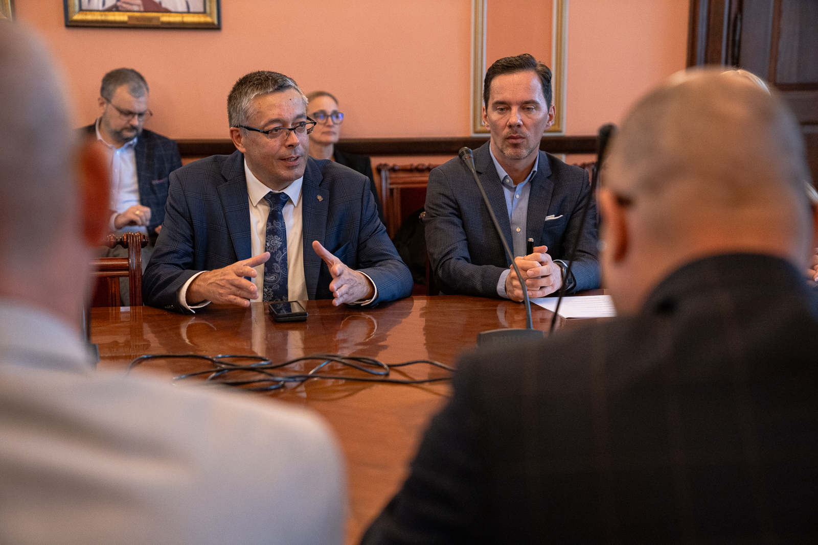 mężczyzna w średnim wieku ubrany w białą koszulę krawat i siwa marynarkę siedzi przy stole