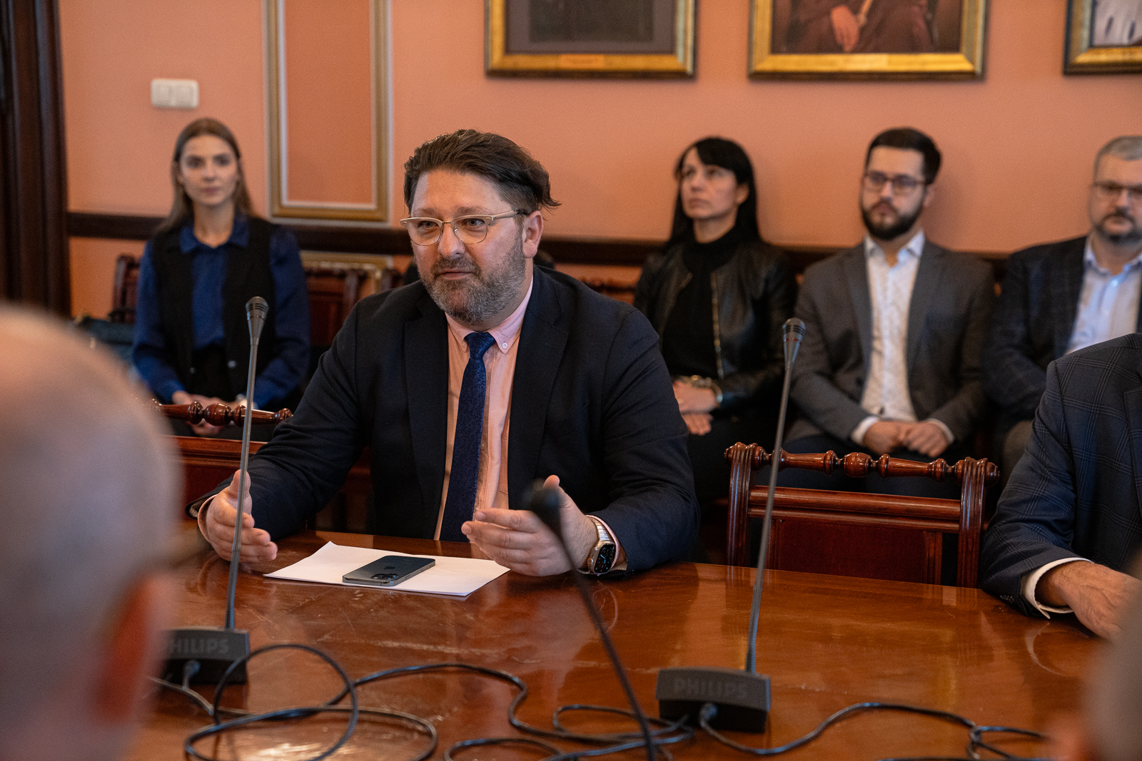 mężczyzna w średnim wieku z zarostem ubrany w różowa koszulę i marynarkę siedzi przy stole