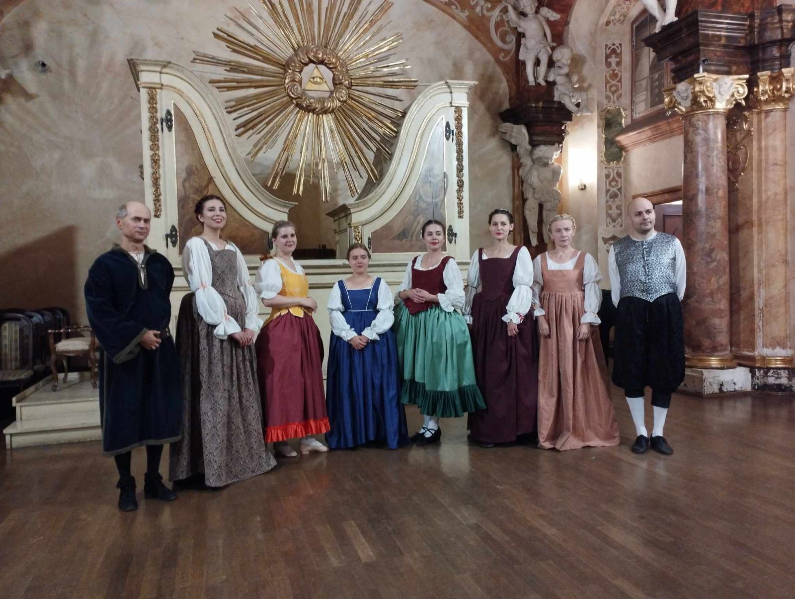Osiem osób w wieku młodym i średnim stoi w rzędzie, ubrani są w stroje z dawnych epok