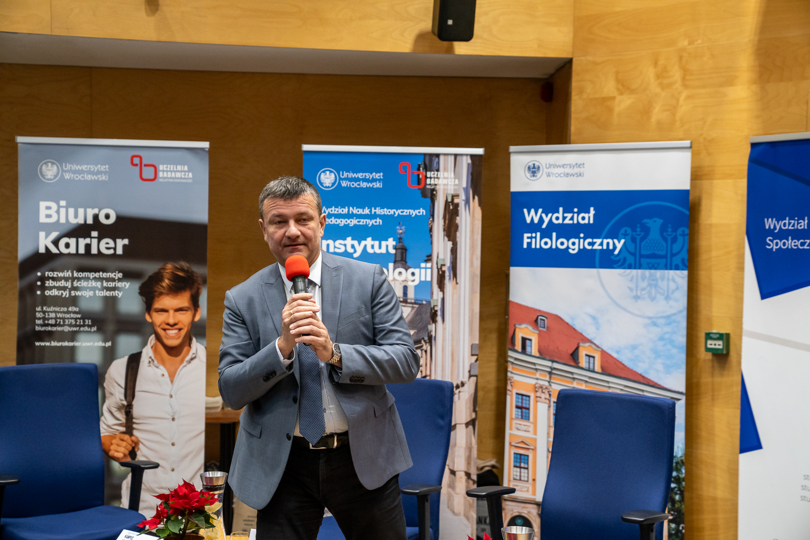 mężczyzna z mikrofonem , za nim banery reklamowe z napisem "Instytut Psychologii" i "Wydział Filologiczny"
