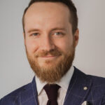 młody mężczyzna z brodą w niebieskiej marynarce w paski, bia łej koszuli i krawacie