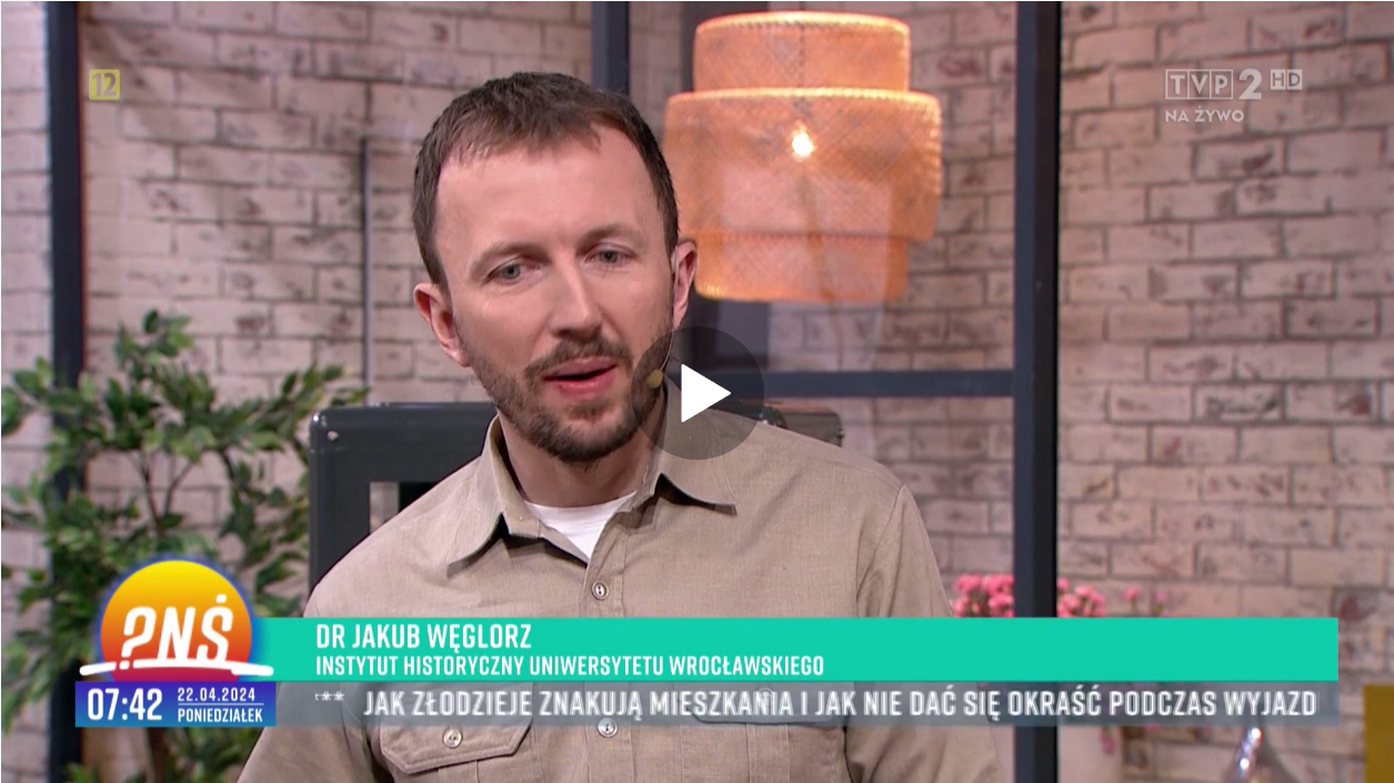 Mężczyzna w średnim wieku, z zarostem na twarzy, z podpisem DR JAKUB WĘGLORZ INSTYTUT HISTORYCZNY UNIWERSYTETU WROCŁAWSKIEGO, w prawym górnym rogu logo TVP2 HD NA ŻYwO