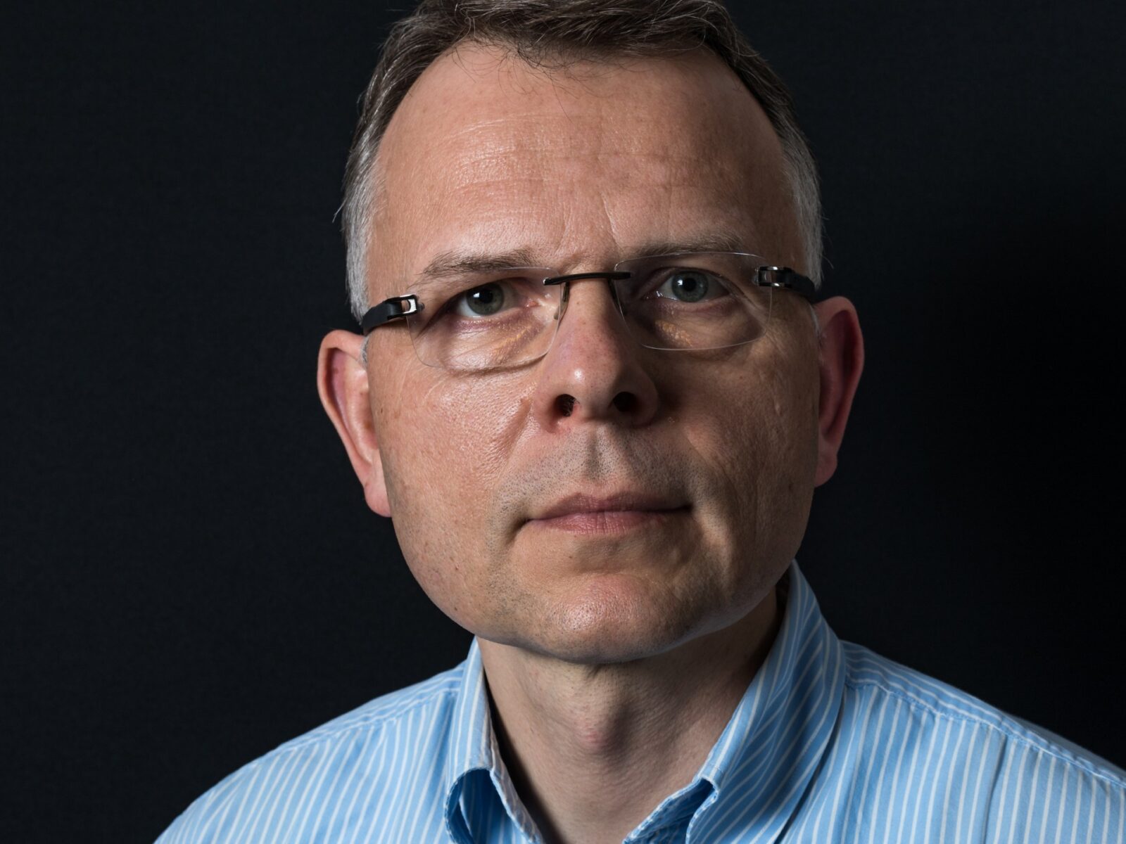 mężczyzna w średnim wieku, ubrany w niebieską koszulę, za nim tło