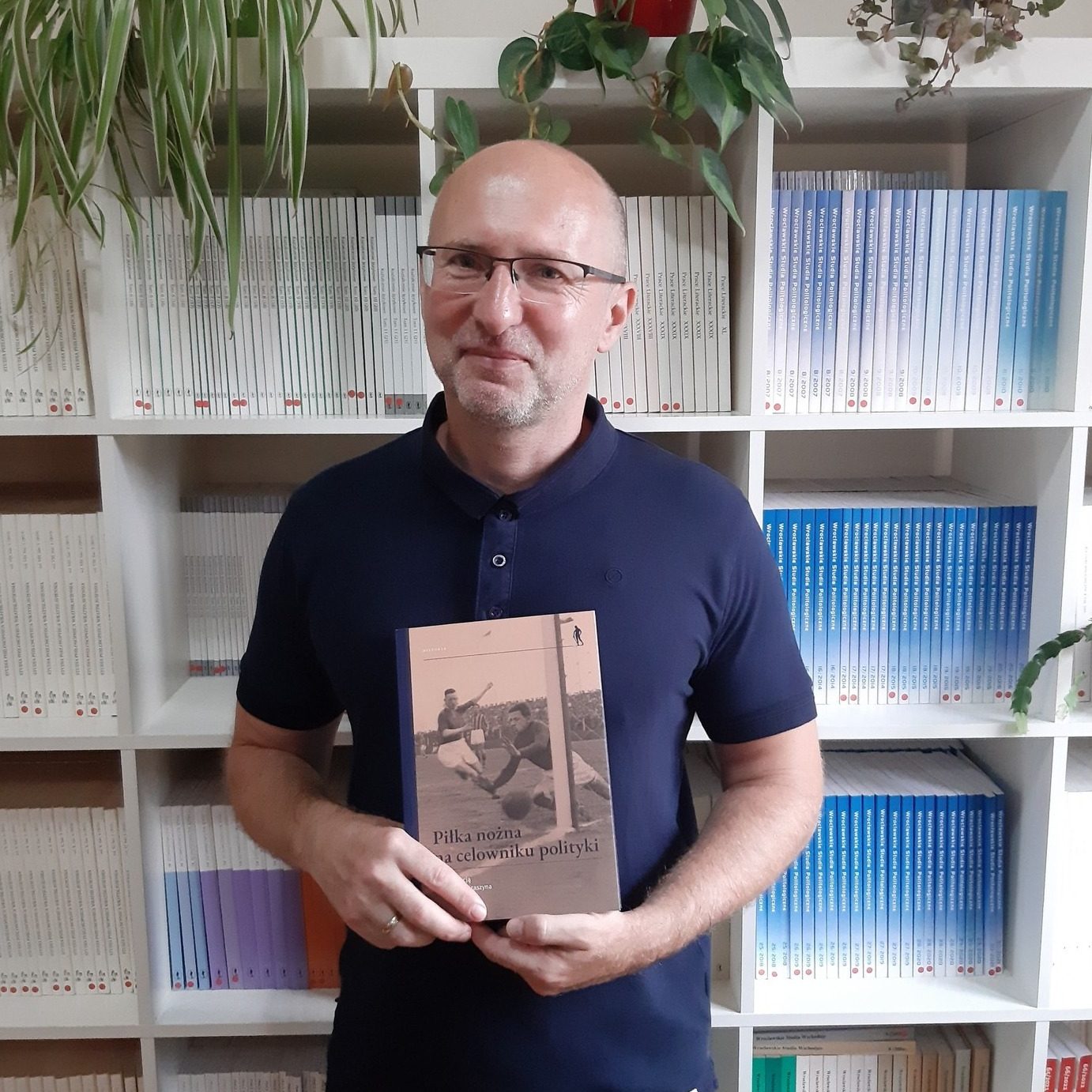 uśmiechnięty mężczyzna z książką na tle regału z książkami