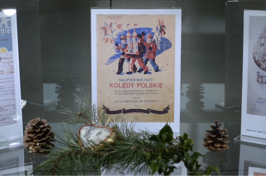 zdjęcie planszy z historycznym tekstem oraz szyszką, zieloną gałazką i wisiorem w kształcie serca ze zdjęciem młodej kobiety