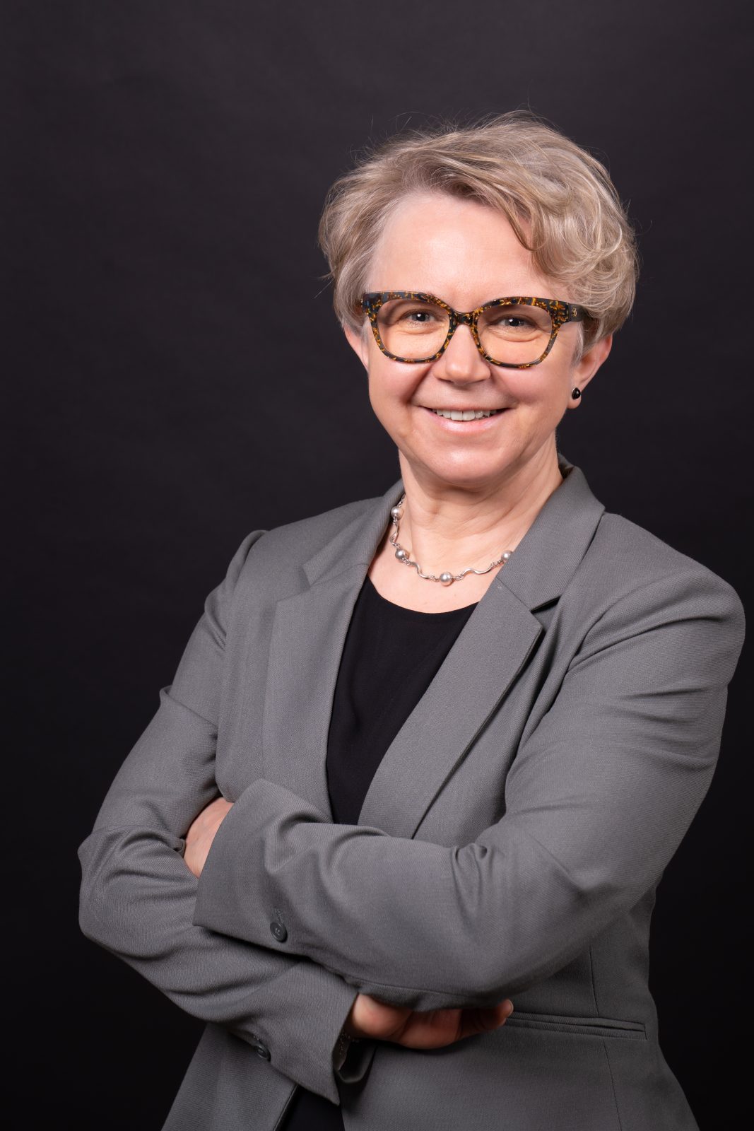 Kobieta ze splecionymi ramionami, krótkimi włosami i w okularach, stojąca na czarnym tle. Dr hab. Irena Barbara Kalla, prof. UWr, członkini Rady UWr na kadencję 2025-2028