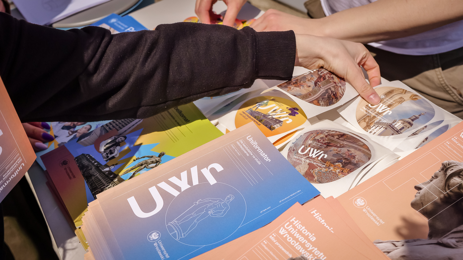 Zdjęcie przedstawia materiały promocyjne UWr i rękę sięgającą po nie.