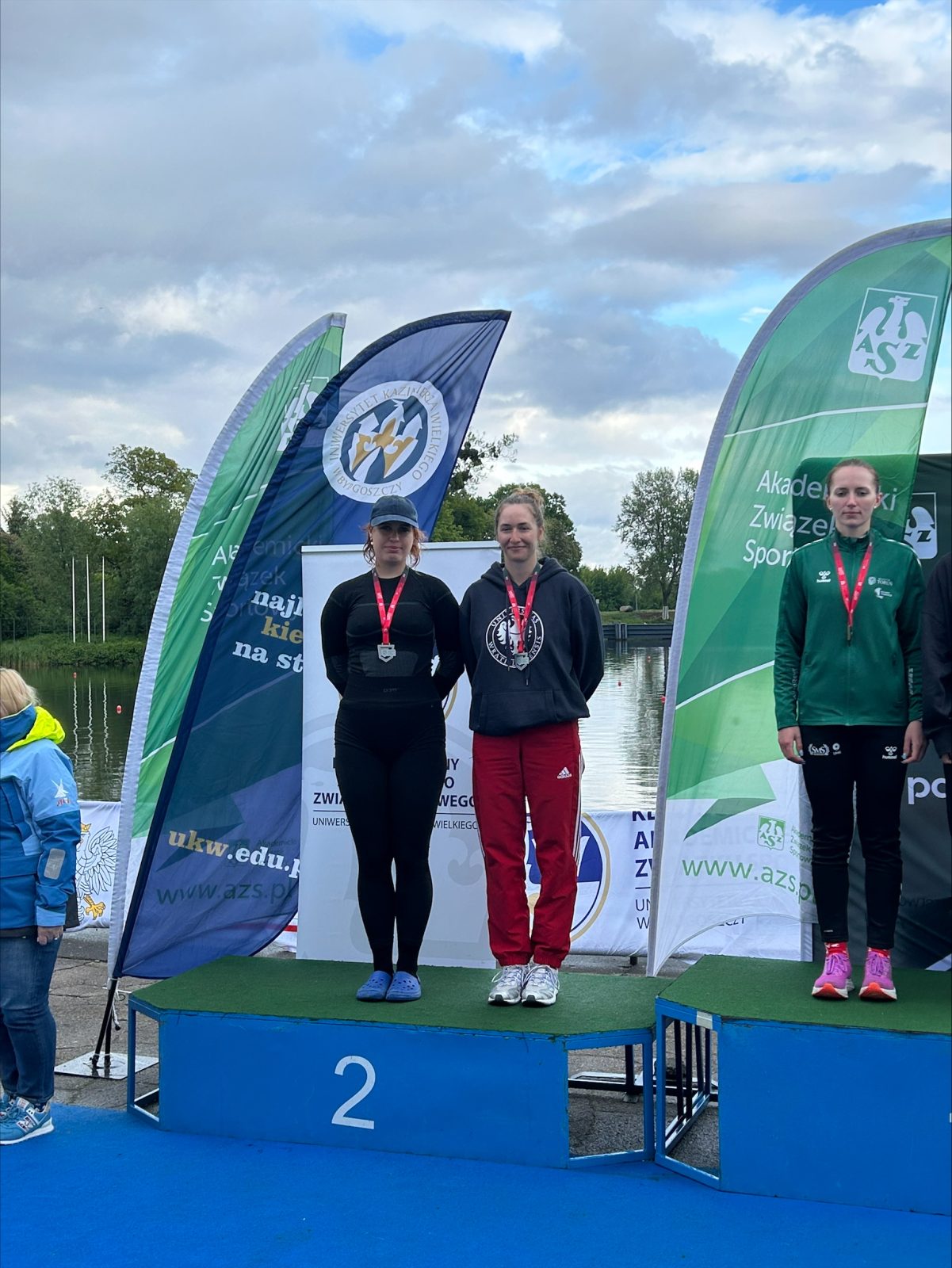 Dwie młode kobiety w strojach sportowych stojące na podium z numerem 2