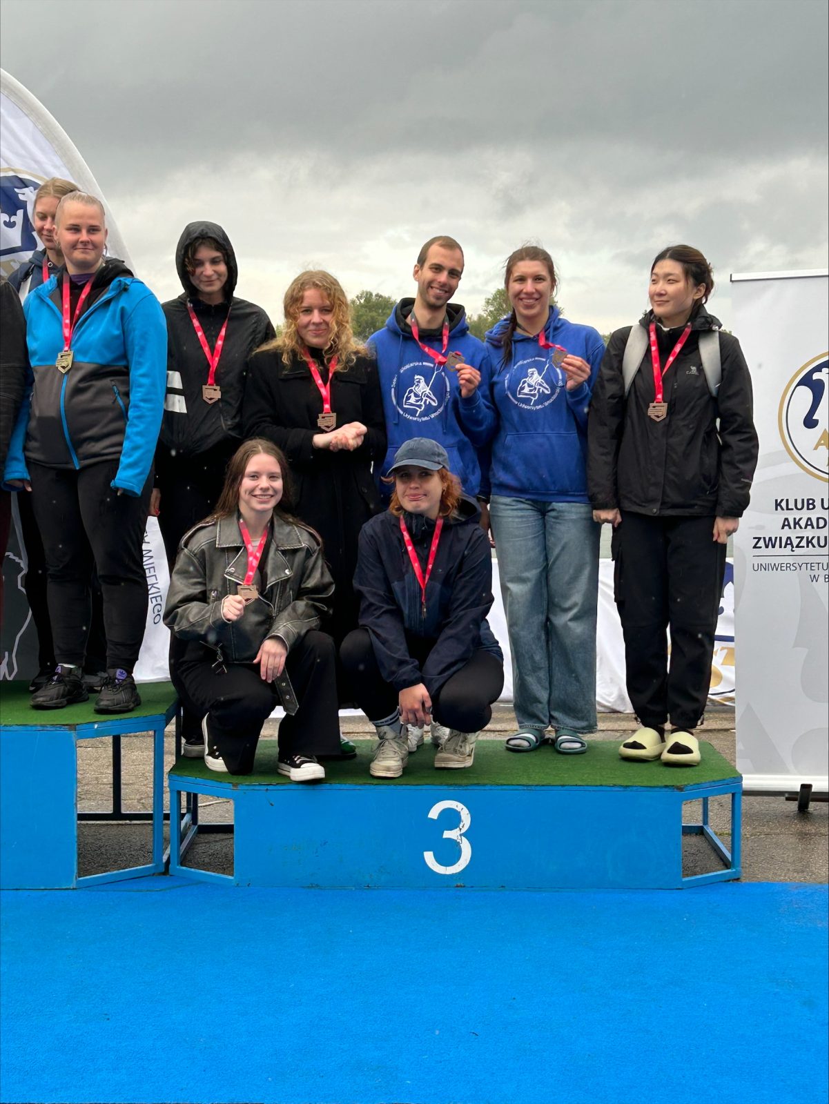grupa siedmiu osób w strojach sportowych stojących na podium z numerem 3