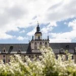 historyczny budynek z wieżą na srodku, przed nim trawa