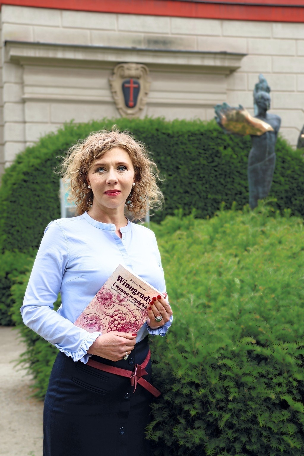 zdjęcie przedstawiające młodą kobietę z książką, ubraną elegancko w ogrodzie