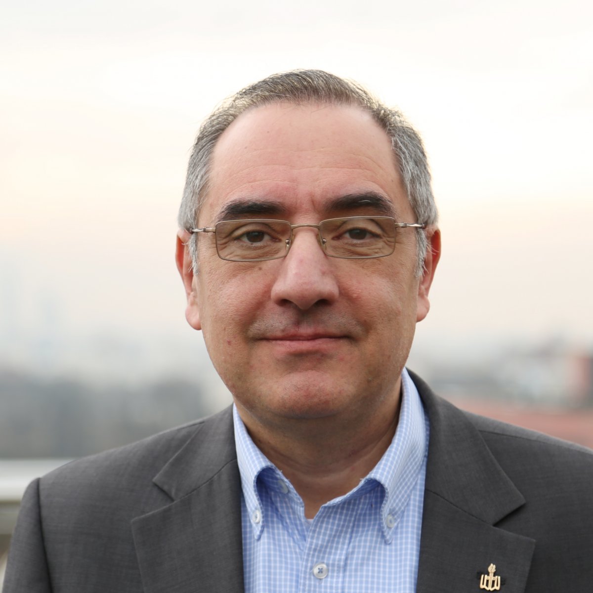 Portret mężczyzny z krótkimi, siwymi włosami, w okularach, w niebieskiej koszuli bez krawata i szarej marynarce