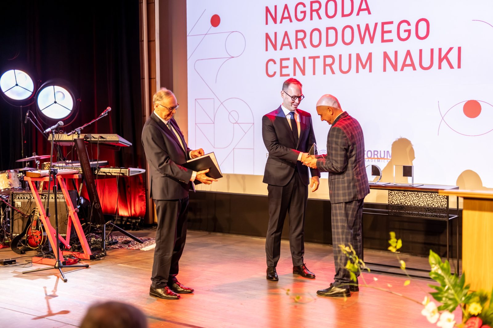 ltrzech mężczyzn w sali konferencyjnej z ekranem z napisem Nagroda narodowego centrum nauki