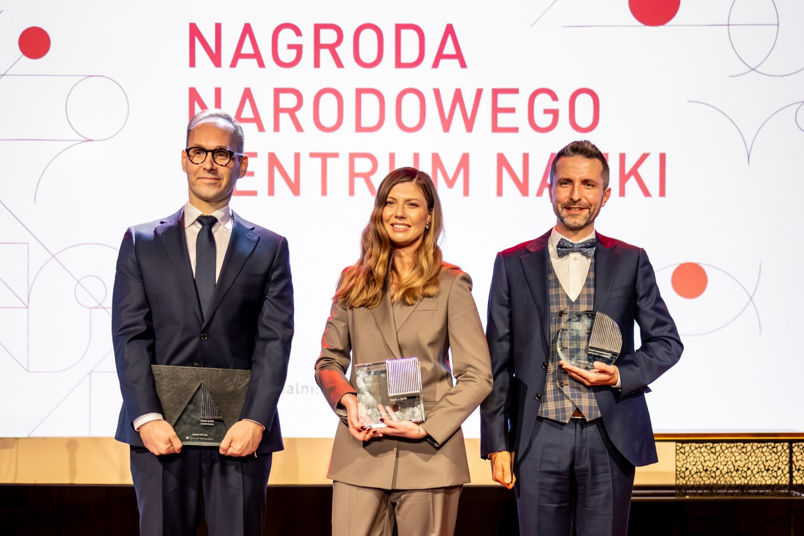 dwóch mężczyzn, miedzy nimi kobieta, za nimi ekran z napisem Nagroda narodowego centrum nauki
