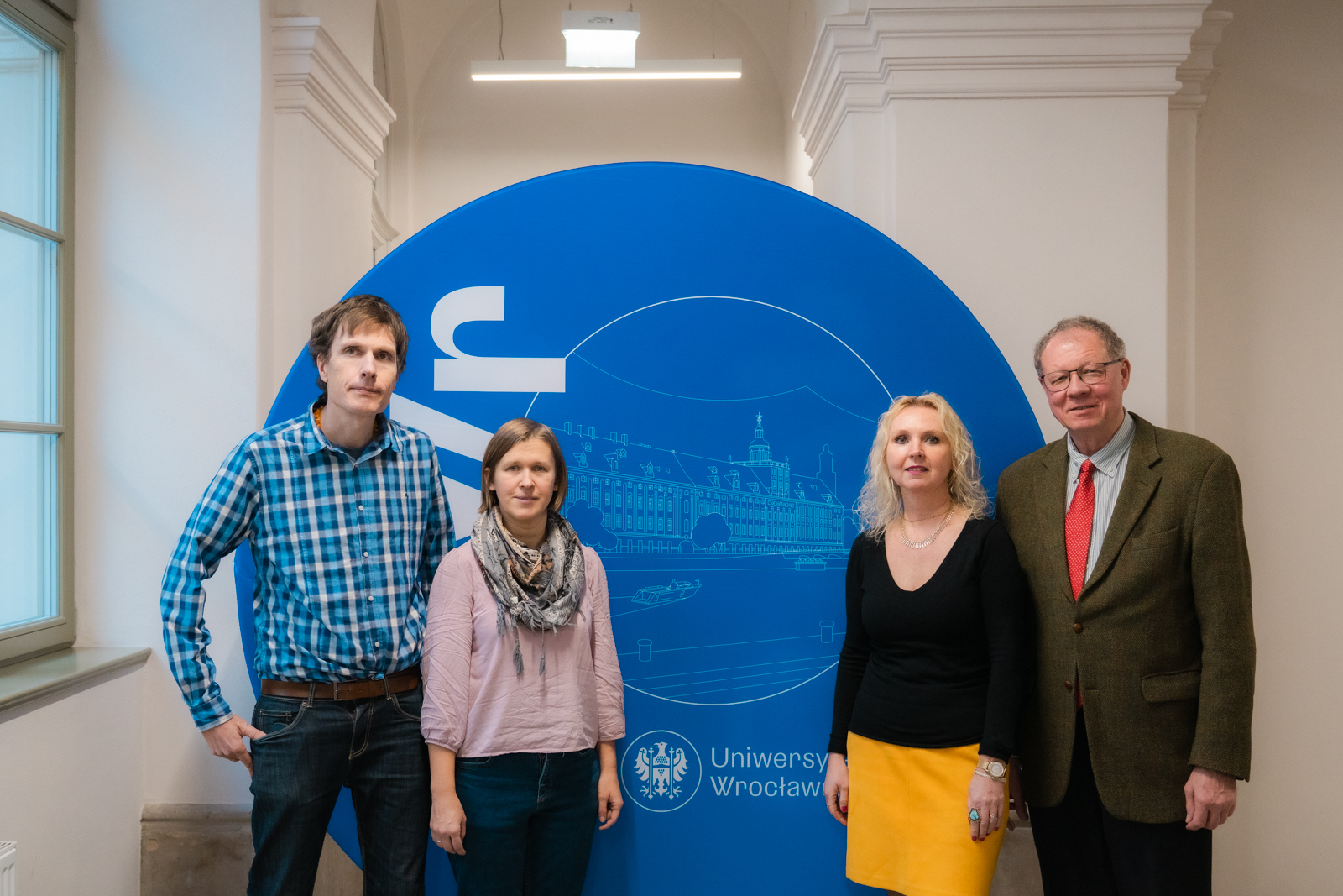 grupa osób stojąca na tle okrągłej, niebieskiej ścianki z logo Uniwersytetu Wrocławskiego